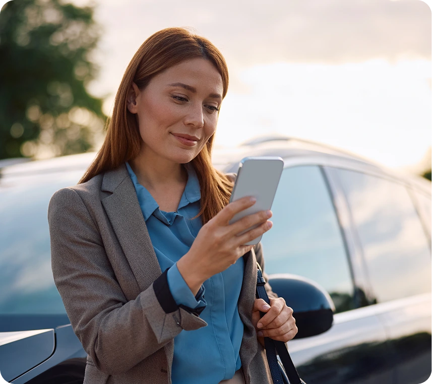 Woman in suit using smartphone outside car.